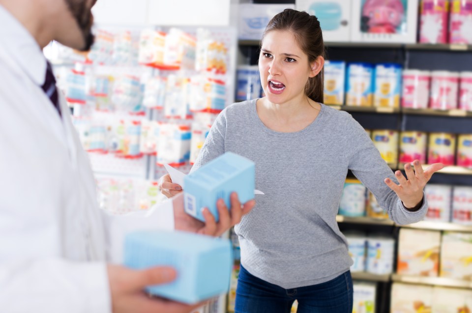 Outraged woman with medicine boxes in a pharmacy.