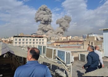 People watch as smoke rises on the skyline after an explosion in Tehran, Iran, on Saturday