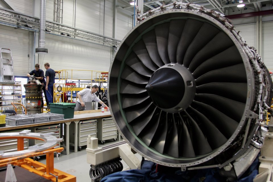 Workers disassembling an aircraft jet engine in a factory.