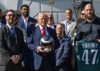 President Donald Trump holds up a helmet, flanked by Philadelphia Eagles tackle #65 Lane Johnson and Philadelphia Eagles head coach Nick Sirianni, as he hosts an event celebrating the Philadelphia Eagles, 2025 Super Bowl champions, at the White House on April 28, 2025, in Washington, D.C.