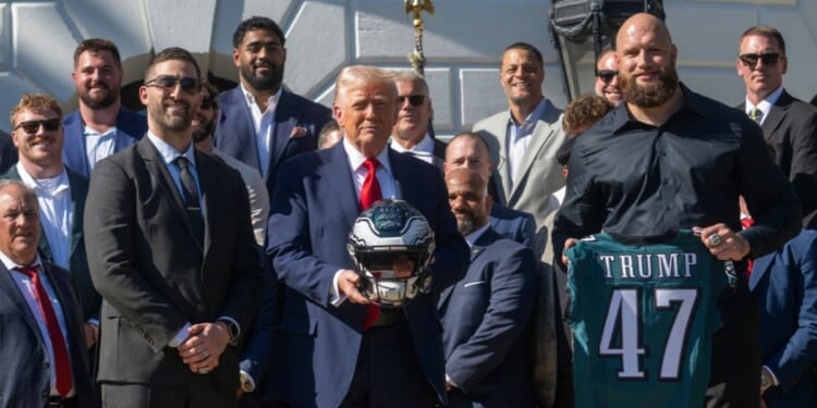 President Donald Trump holds up a helmet, flanked by Philadelphia Eagles tackle #65 Lane Johnson and Philadelphia Eagles head coach Nick Sirianni, as he hosts an event celebrating the Philadelphia Eagles, 2025 Super Bowl champions, at the White House on April 28, 2025, in Washington, D.C.
