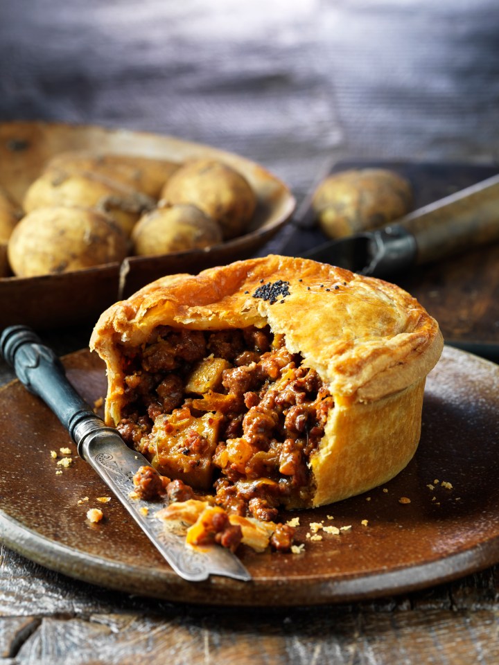 Meat and potato pie with a crust cut to reveal the filling, a knife, and potatoes in the background.