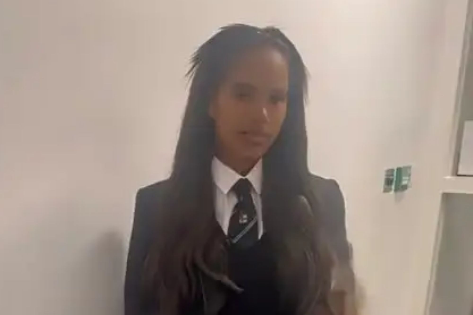 An image collage containing 1 images, Image 1 shows A young woman in a dark suit with a white shirt and tie stands in a hallway