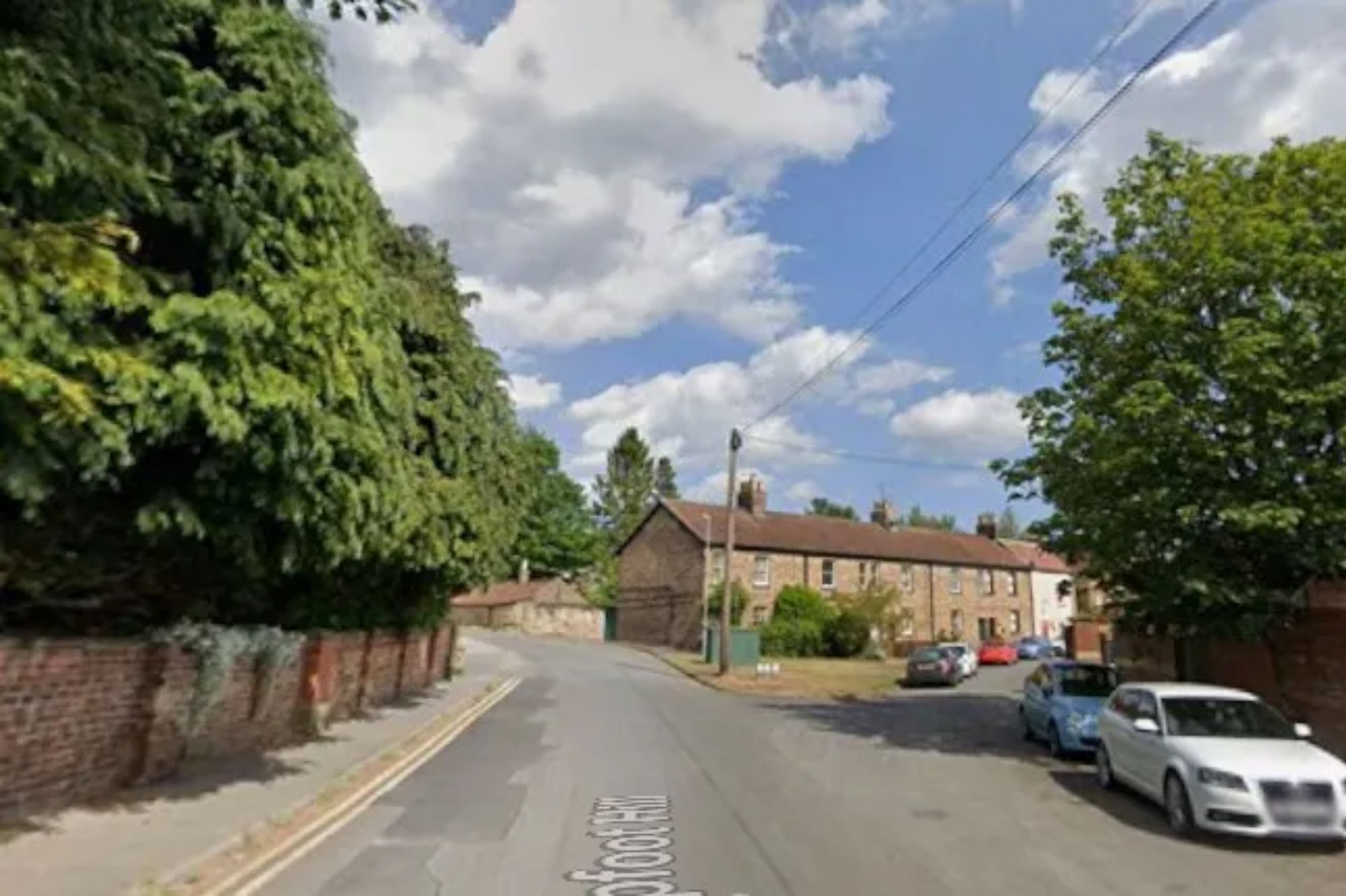 An image collage containing 1 images, Image 1 shows Street view of a road with parked cars, brick houses, and lush trees under a cloudy sky