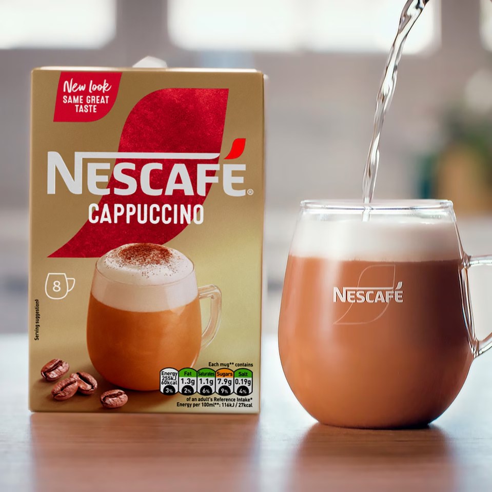 Nescafe Cappuccino instant coffee box next to a mug of prepared cappuccino with water being poured into it.