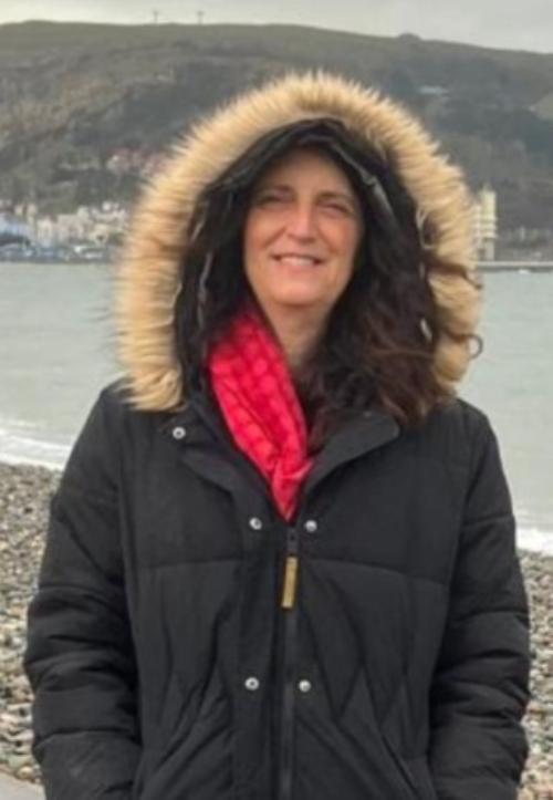 Eleanor from Staffordshire Police, smiling and wearing a black winter coat and red scarf by a body of water.