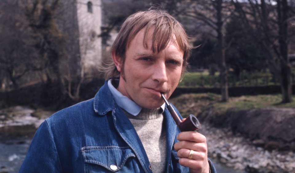 Eric Allan as Frank Blakey, holding a pipe.
