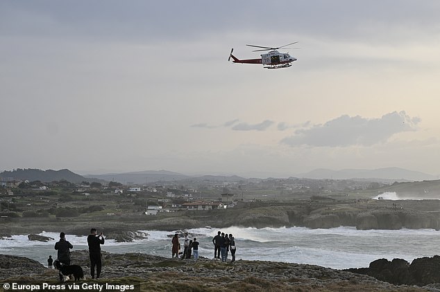 Around 70 people are understood to be working to complete the mission before nightfall. Pictured: A rescue helicopter at the scene, as bystanders watch on
