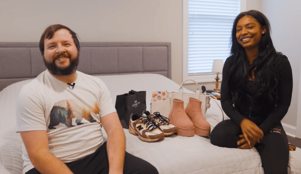 A man and a woman sitting on a bed with new shoes and a bag.