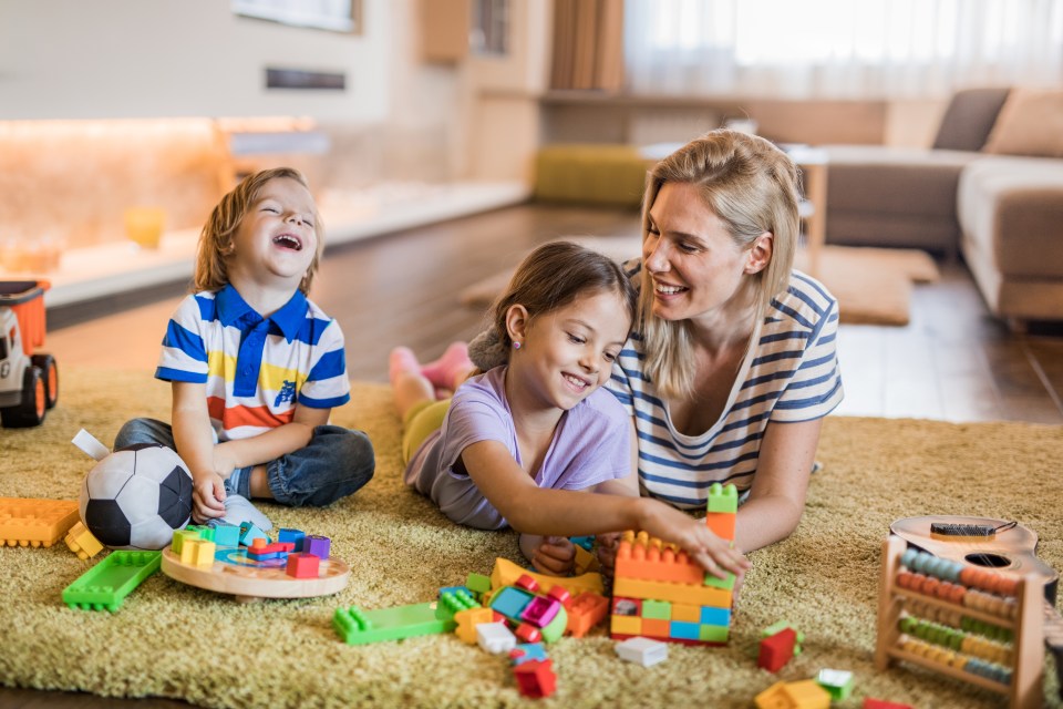 Mother and children playing with toys on a carpet in the living room.