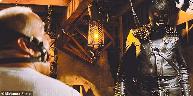 Emerging from a locked box, the eerie figure is dressed head-to-toe in a black leather bondage suit with a zippered mask and leash