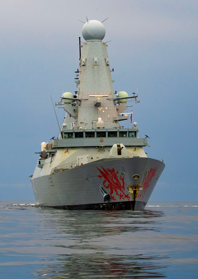 HMS Dragon, a gray warship with a red dragon painted on its bow, sails on the water.