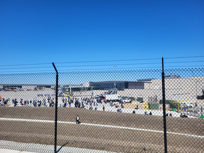 Crowd of people behind a chain-link fence at an airport.