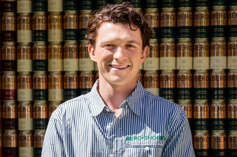 Tom Holland smiling in front of a wall of BERO cans.