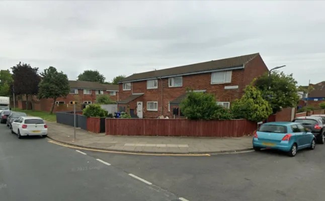 Residential street with brick row houses and cars parked along the curb.