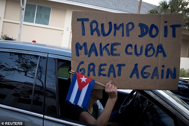 A woman holds a sign and Cuban flags as supporters of Trump participate in a protest against Cuba's government, in Miami, Florida, last month