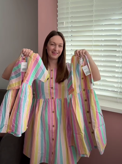 A woman wearing a striped dress holds up two smaller matching dresses.