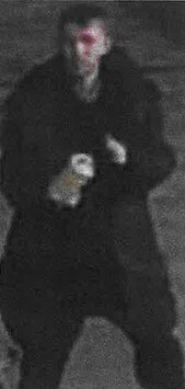 CCTV image of a man in a dark coat, with a blurry red area around his face and holding a light-colored object.