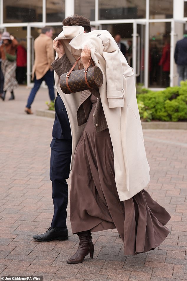 A woman uses her glamorous coat to protect her hair from the rainy conditions at Cheltenham