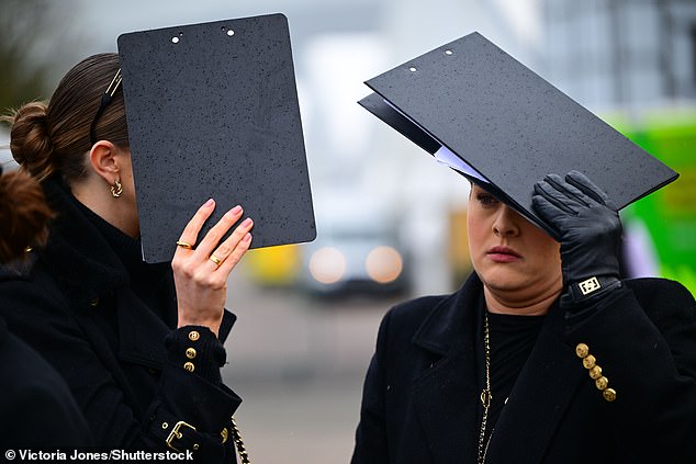 Getting creative! Racegoers seek shelter from the rain under clipboards at the racing event