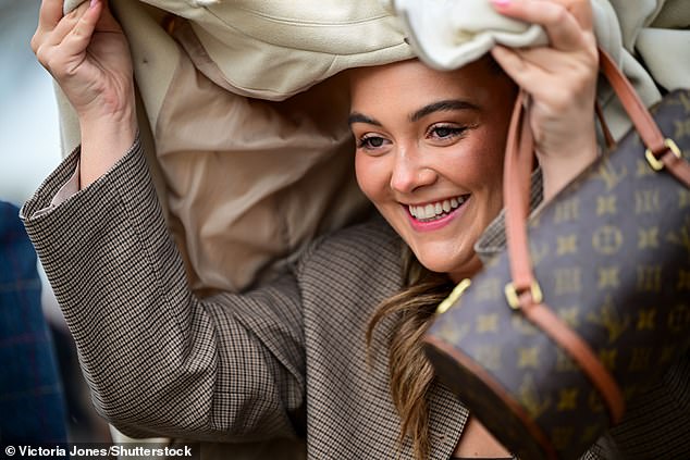 A racegoers covers her head with her jacket as she seeks shelter from the rain at the festival