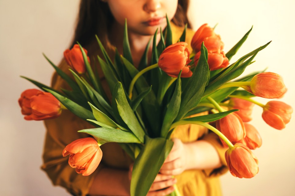 Teenage girl in a yellow dress holding a bouquet of orange tulips.