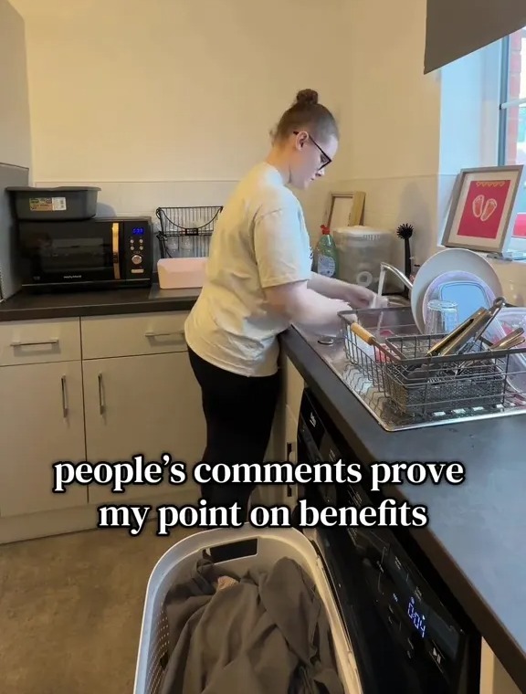 A person with a bun and glasses washing dishes in a kitchen.