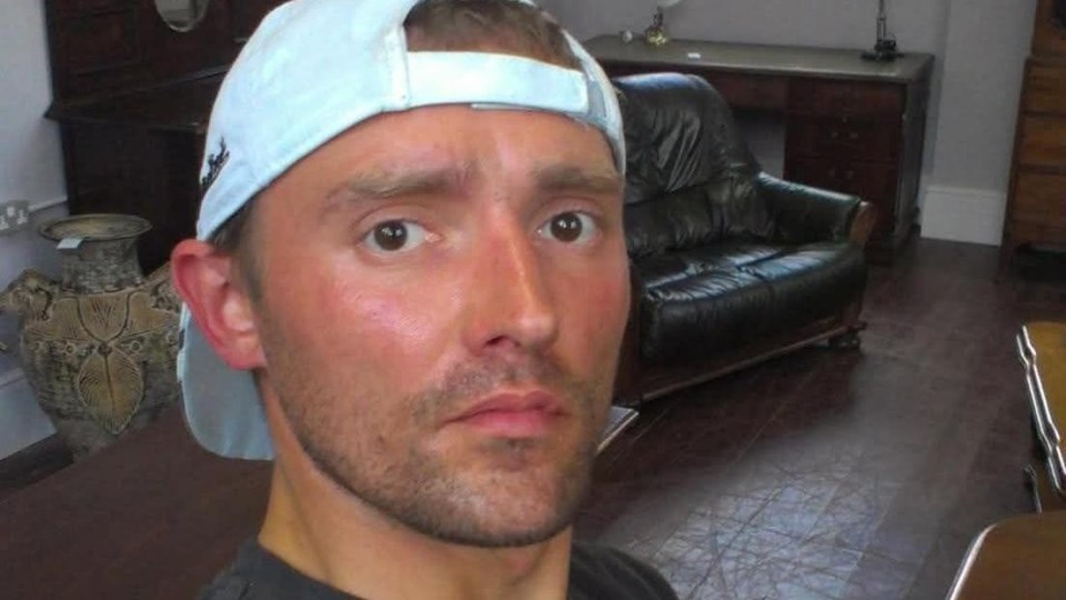 A man wearing a light blue baseball cap backward looks directly at the camera.