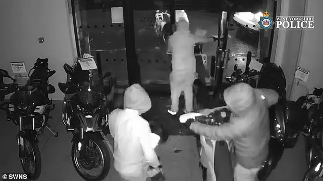 Six hooded people in tracksuits wheel out nine off-road motorbikes, pushing another bike over in the process