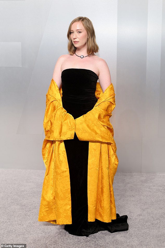 30, best known for her role in the HBO Max series Hacks, slipped into a clashing combination of black gown and a garish yellow wrap around that looked awkward to hold