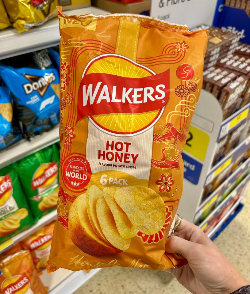 A hand holds a bag of Walkers Hot Honey crisps in a grocery store.
