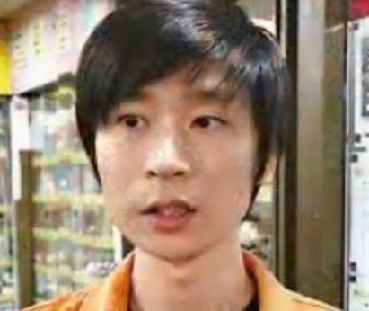 Headshot of an Asian man with short dark hair, wearing an orange collared shirt.