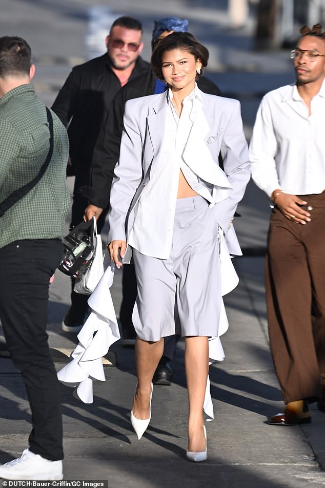 When the biracial beauty first arrived to the studio with her left hand hidden, she bared her belly in a grey blazer over a white cropped blouse featuring ruffled tendrils, grey formal shorts and white pumps