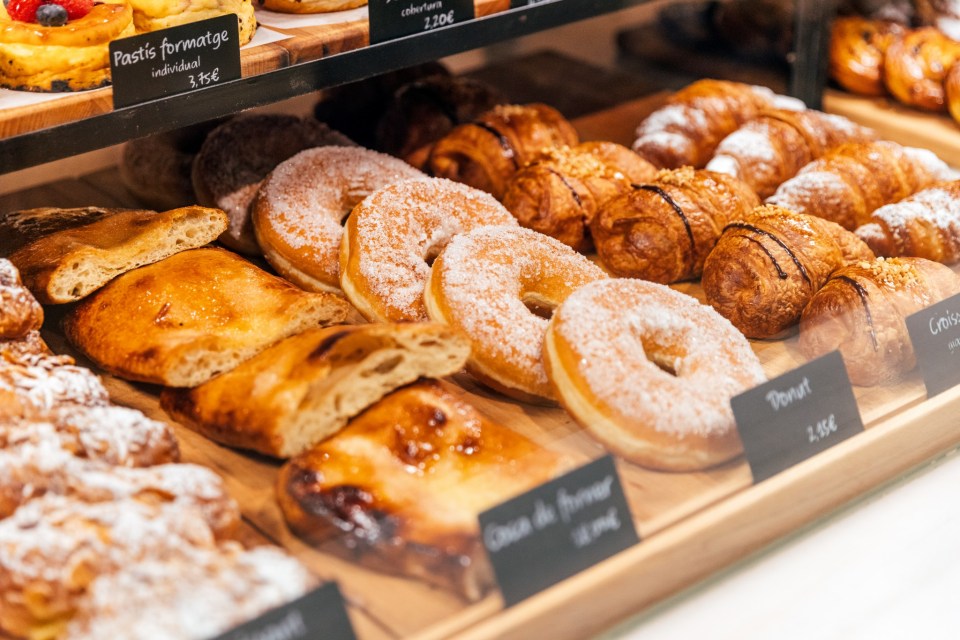Assortment of fresh pastries, including donuts, croissants, and other sweet baked goods, displayed in a bakery with price tags.