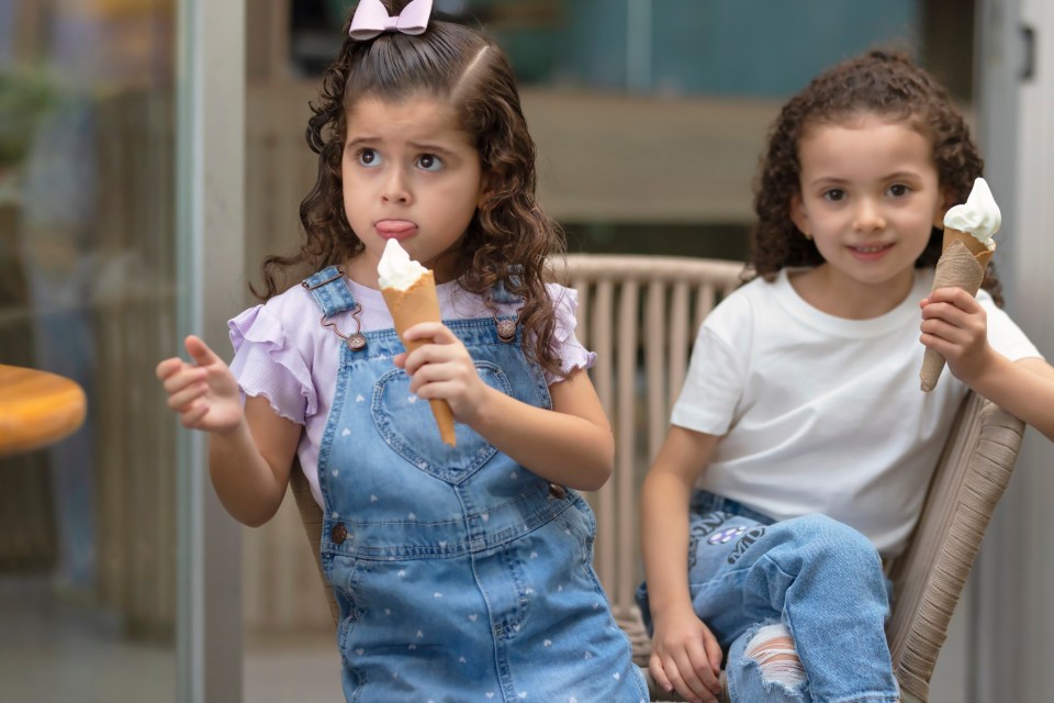 Two young girls sitting in chairs holding ice cream cones.