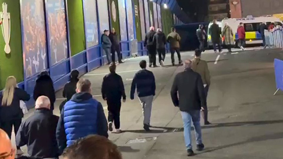 Chelsea fans walking near a stadium entrance, with a police van in the background.