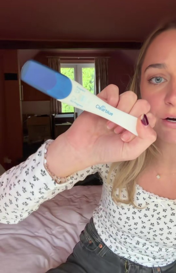 A woman holds up a Clearblue pregnancy test, showing a positive result.