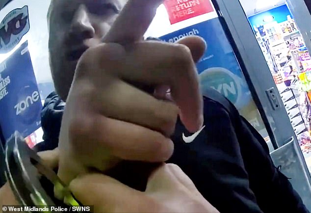 But once they have ensured the knife is securely out of the way, only then do the unconvinced constables lift the shutters, not to free him - but to immediately cuff him (pictured)