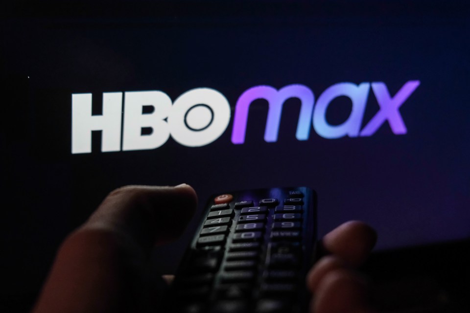 Hand holding a TV remote with the HBO Max logo displayed on a screen.