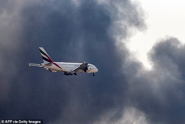 An Emirates Airbus A380 aircraft prepares for landing as a smoke plume rises from an ongoing fire near Dubai International Airport on March 16