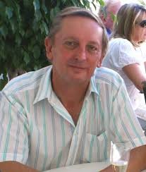 A man with short blonde hair and a striped shirt smiles at the camera.