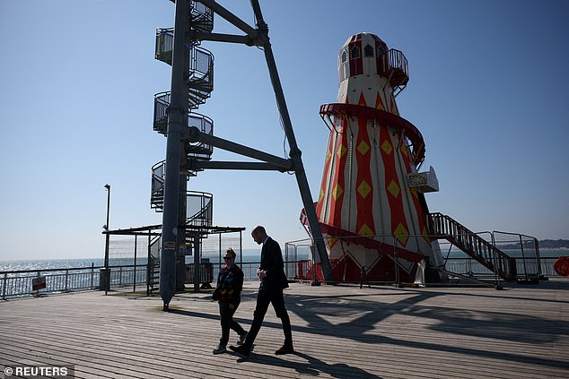 Enjoying the spring weather, the royal was dapper in a black suit and tie as he walked along the seaside, passing a Ferris wheel and Helter Skelter to talk to wellwishers