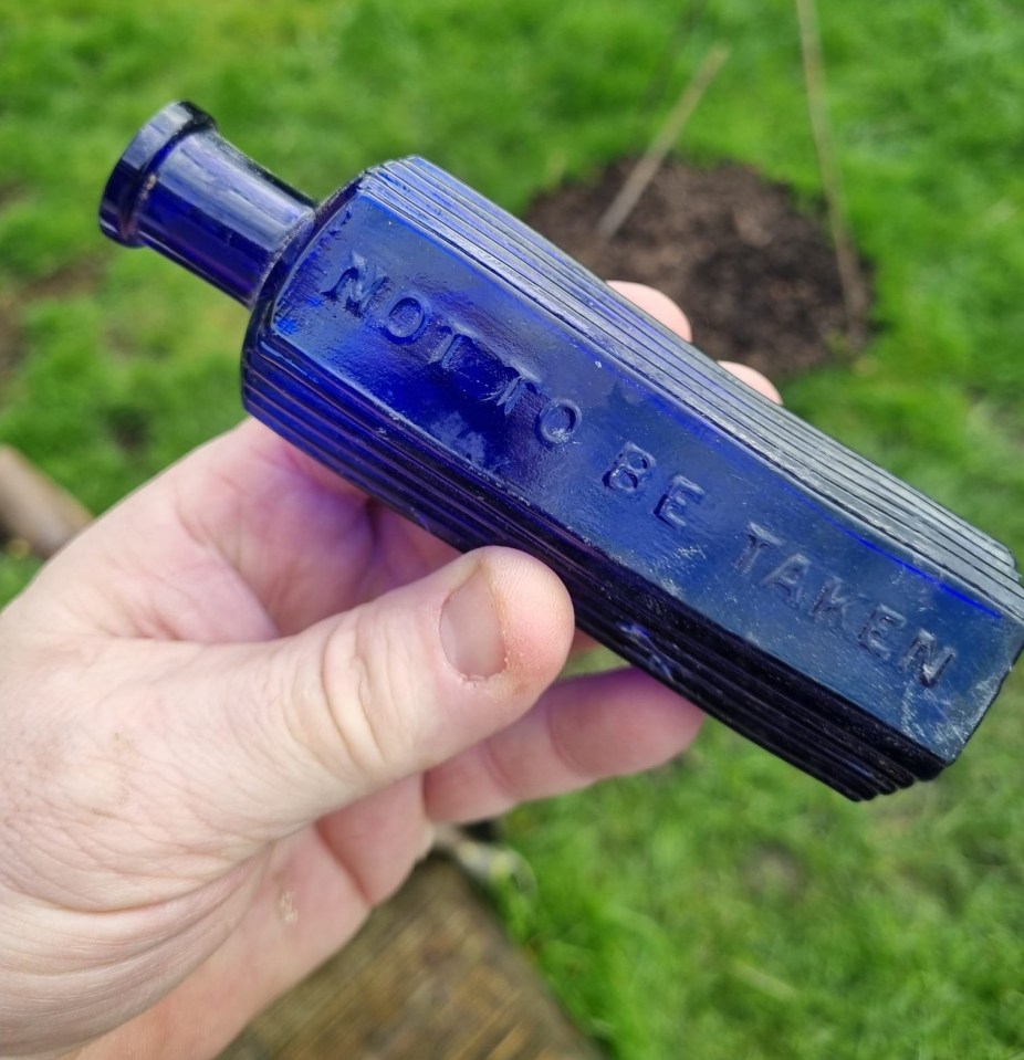 Hand holding a cobalt blue antique poison bottle with "NOT TO BE TAKEN" embossed on its ribbed side.