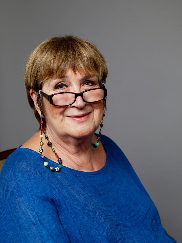 Dame Jenni Murray in a blue top with glasses and a colorful beaded necklace.