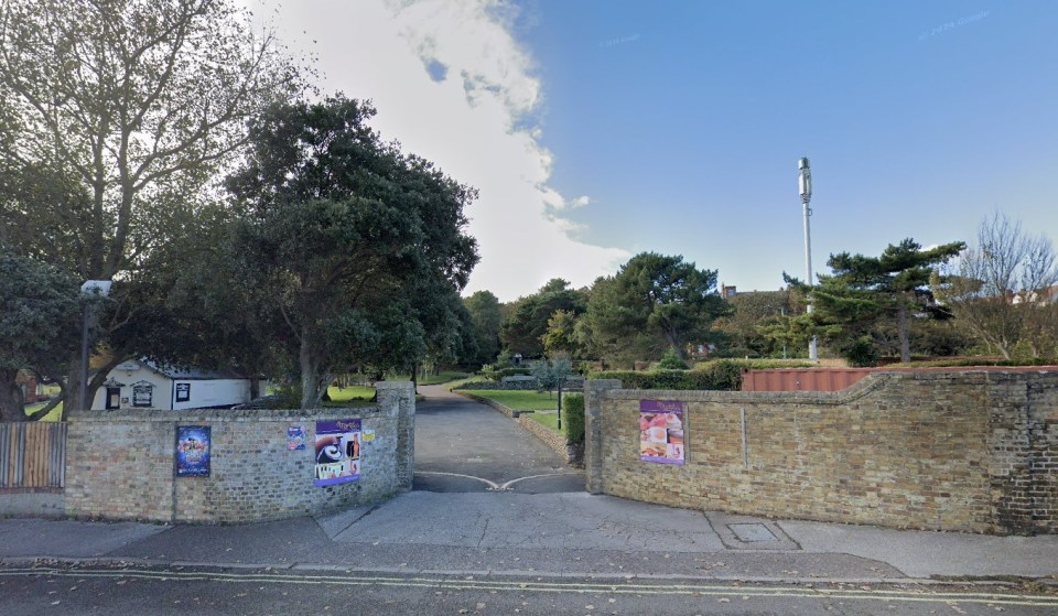 Entrance to Sparrows Nest Gardens in Lowestoft, with a paved path leading into a park-like area with trees and a building in the background.