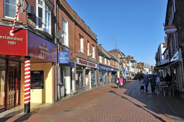 A street lined with shops, including a barber shop with a red and white striped pole, on a sunny day.