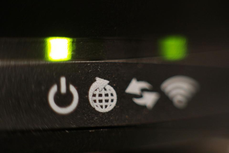 Close-up of a broadband internet router's front panel, showing illuminated green lights and white icons for power, globe, and Wi-Fi.