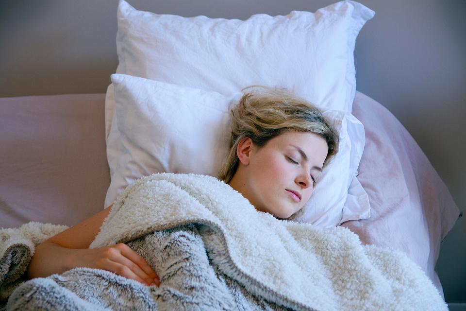 Woman sleeping soundly in bed with a fluffy blanket.
