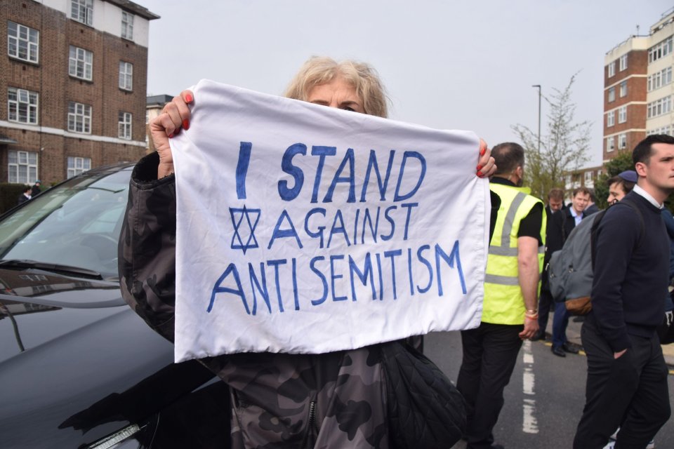 A woman holding an 'I stand against antisemitism' banner.