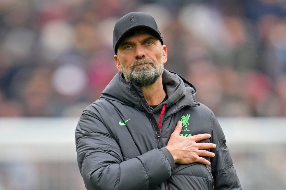 Liverpool soccer manager Jürgen Klopp wearing a black cap and jacket with the team's green emblem, his right hand over his heart.